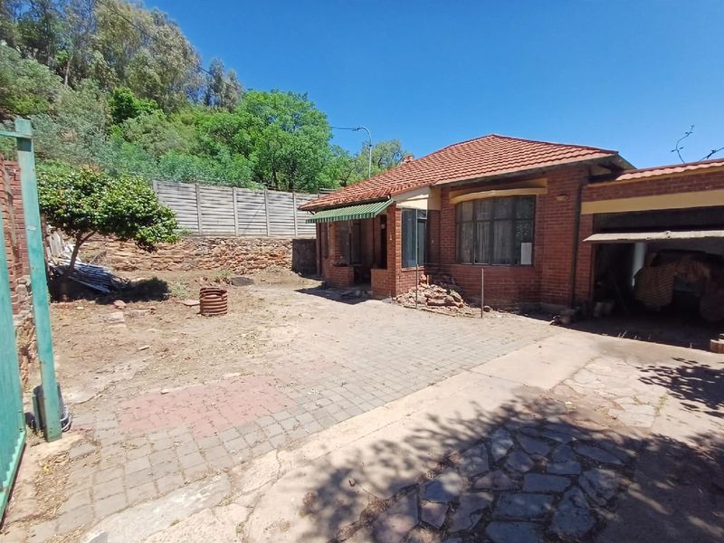 Rear view of a brick house featuring a tiled roof, attached garage, and a paved courtyard area with a retaining wall.