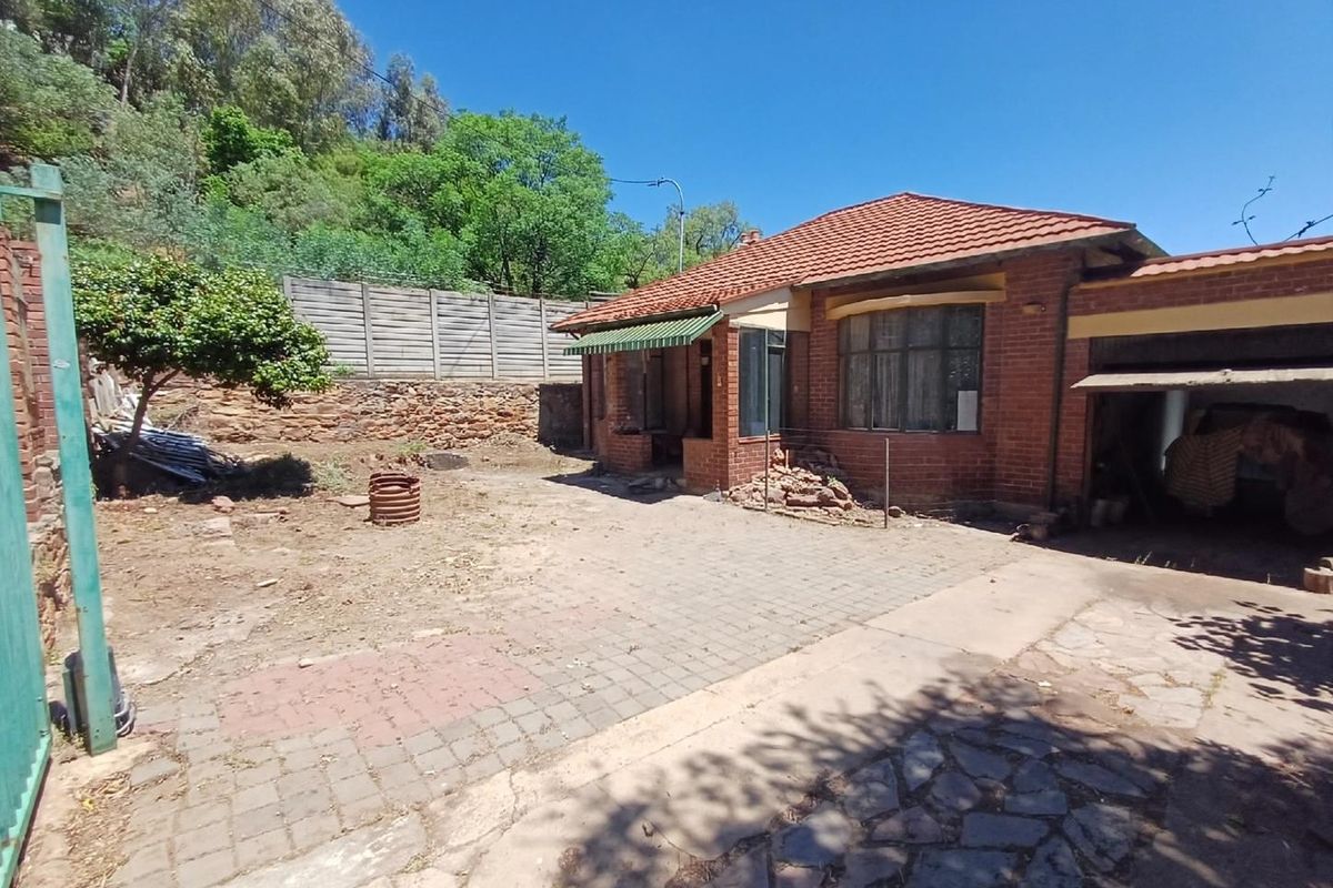 Rear view of a brick house featuring a tiled roof, attached garage, and a paved courtyard area with a retaining wall.