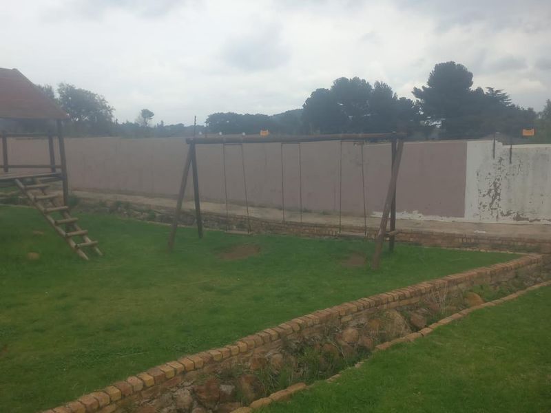 A private garden area featuring a lawn, brick retaining wall, and wooden play equipment, enclosed by a perimeter wall requiring maintenance.