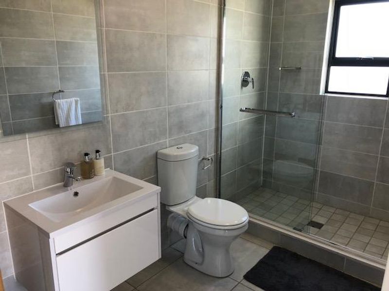 Modern bathroom featuring a wall-mounted vanity, a glass-enclosed shower, and neutral grey wall and floor tiling.