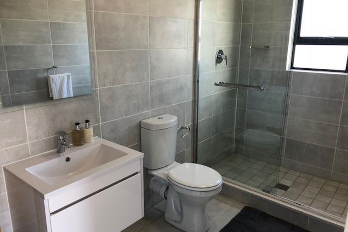 Modern bathroom featuring a wall-mounted vanity, a glass-enclosed shower, and neutral grey wall and floor tiling.