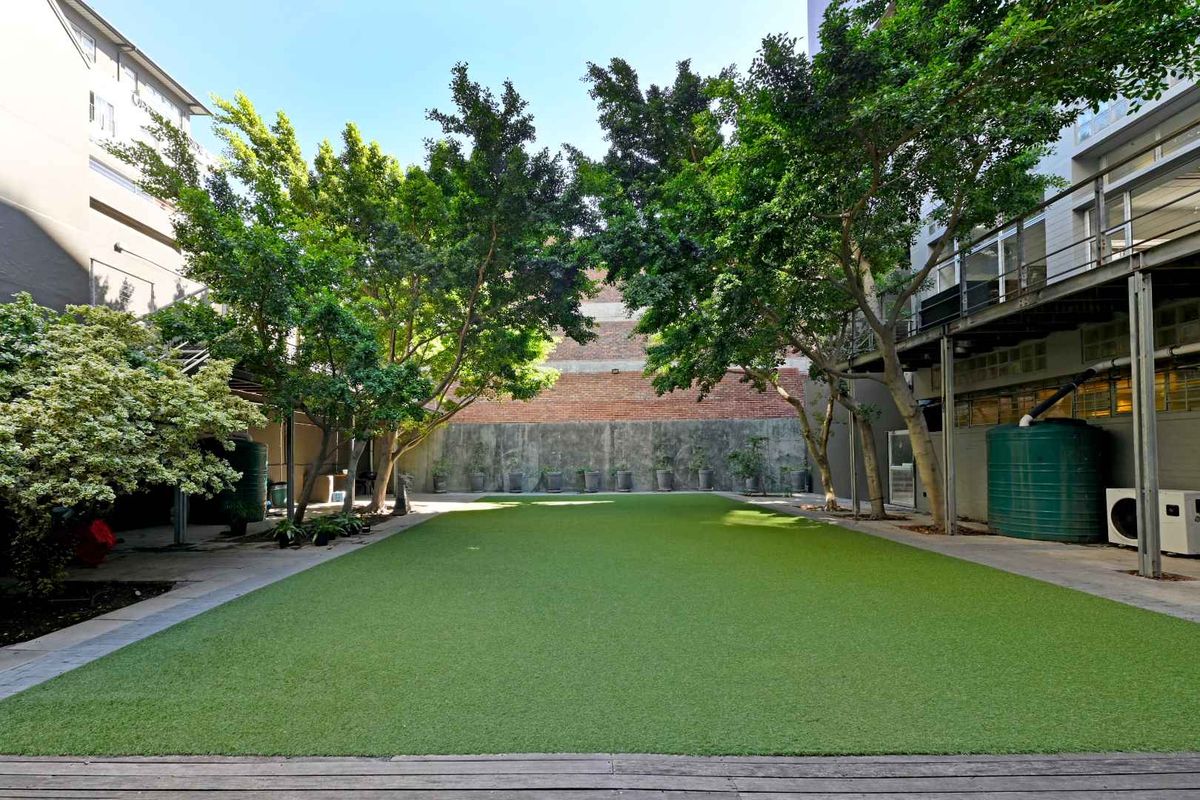 A well-maintained communal courtyard featuring artificial turf, mature trees, and paved walkways between apartment building wings.