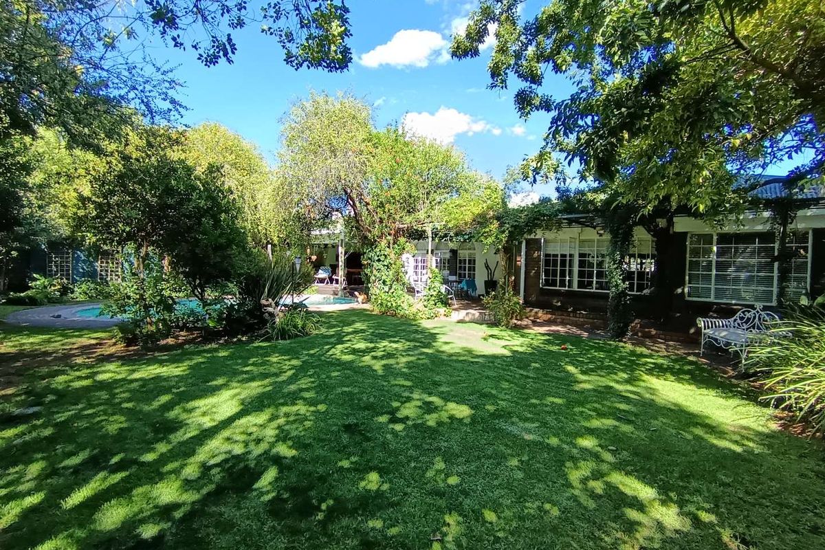 A lush, well-maintained rear garden featuring a manicured lawn, mature trees, and a swimming pool area adjacent to the home's exterior.