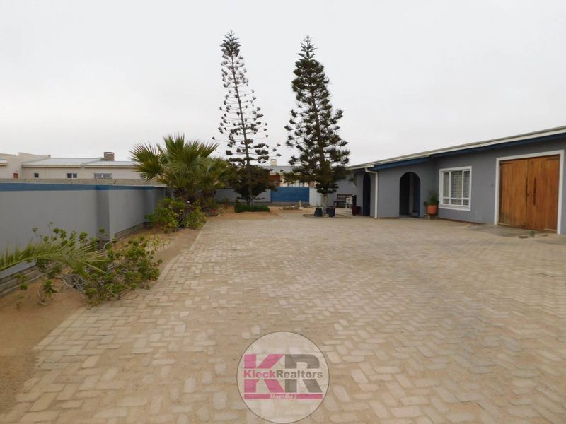 Spacious front exterior featuring a large paved driveway, boundary wall, and a double wooden garage door entrance.