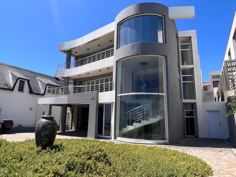 Modern multi-story residential facade featuring a prominent curved glass tower, stainless steel balcony railings, and paved driveway access.
