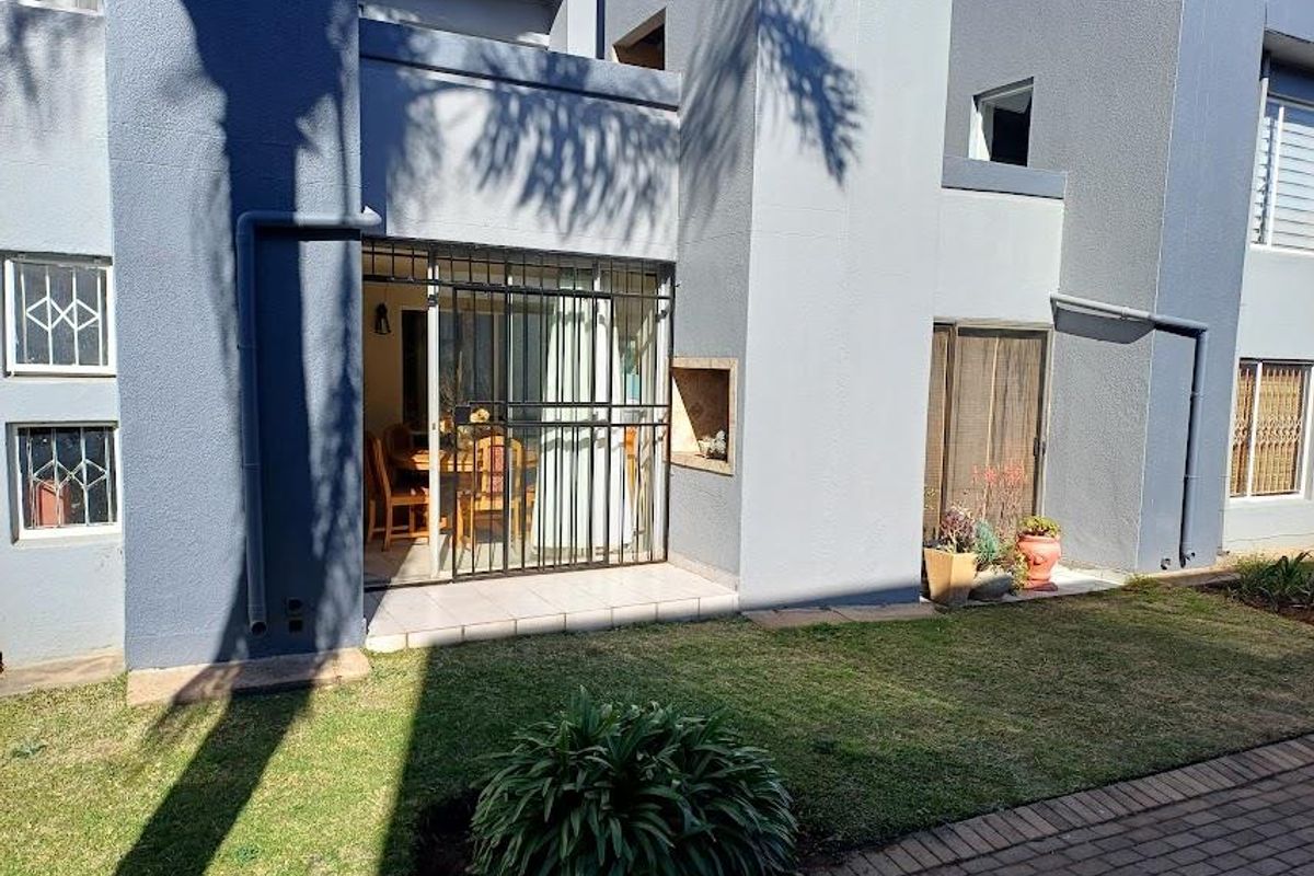 Rear exterior view of the townhouse featuring a small garden, paved walkway, and a patio area with a built-in braai and security gate.
