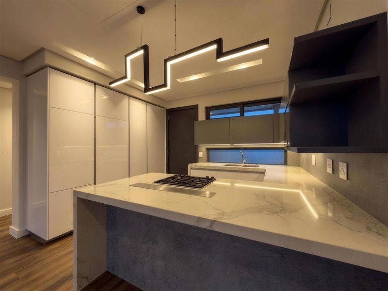 Modern kitchen featuring high-gloss cabinetry, marble-look stone countertops, integrated gas hob, and contemporary geometric pendant lighting in a sleek, minimalist design.