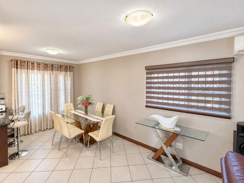 An open-plan living and dining area featuring neutral wall tones, tiled flooring, modern window treatments, and an integrated air conditioning unit.