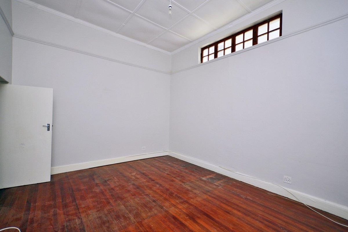 An empty bedroom featuring original timber flooring, high ceilings with decorative cornicing, and a high-set clerestory window for natural light.