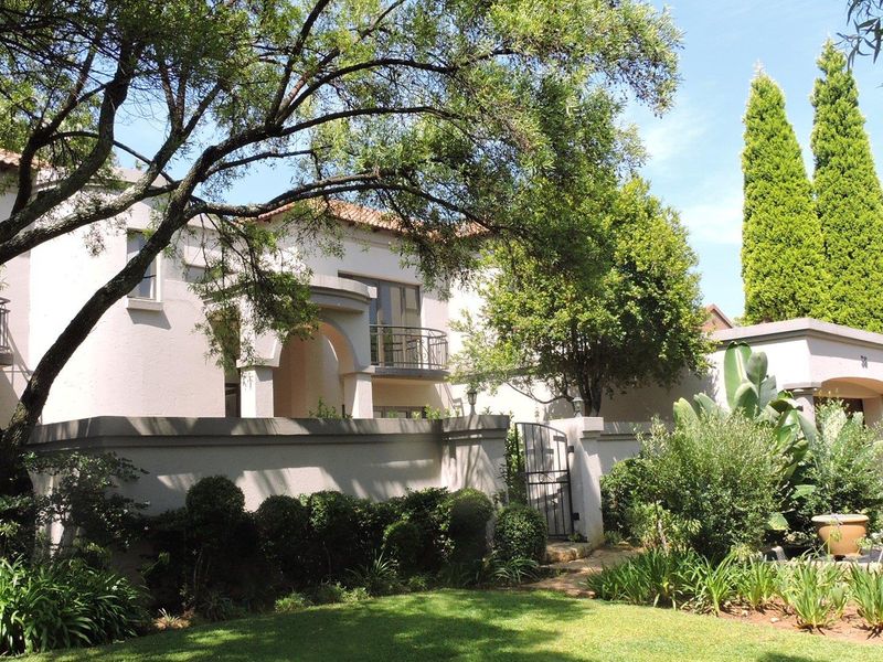 Front elevation of a two-story residence featuring a terracotta tiled roof, arched entrance portico, and wrought iron balcony railings set within a landscaped garden.