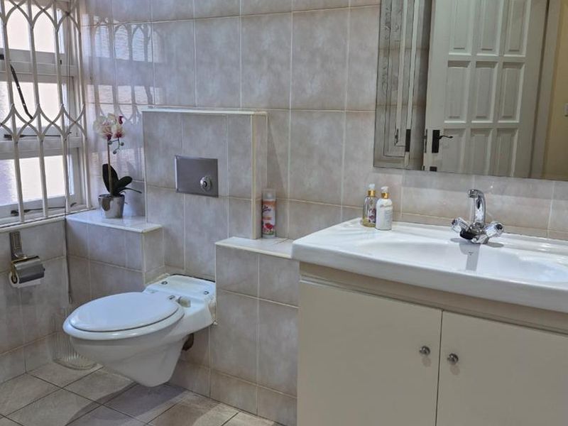 A functional bathroom featuring a wall-mounted toilet, vanity cabinet with basin, and full-height wall tiling.