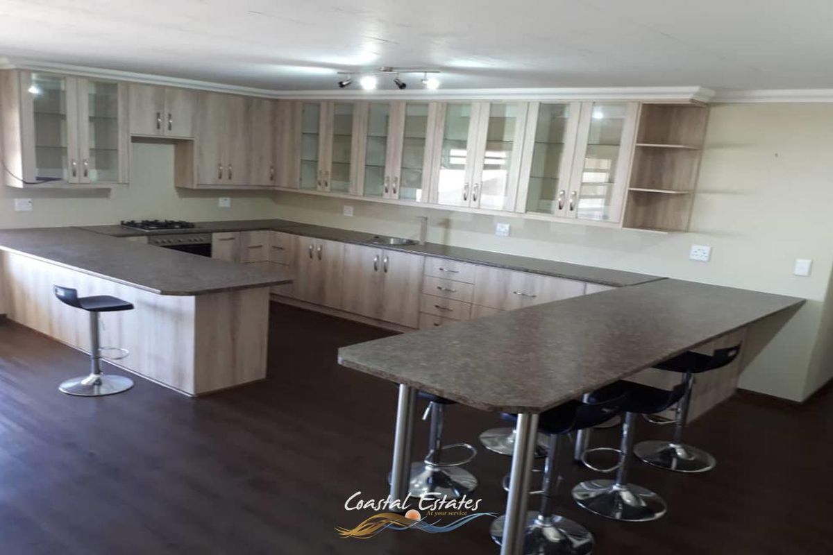 Spacious kitchen featuring light wood cabinetry, glass-fronted display cabinets, dark laminate countertops, and a large breakfast bar island.
