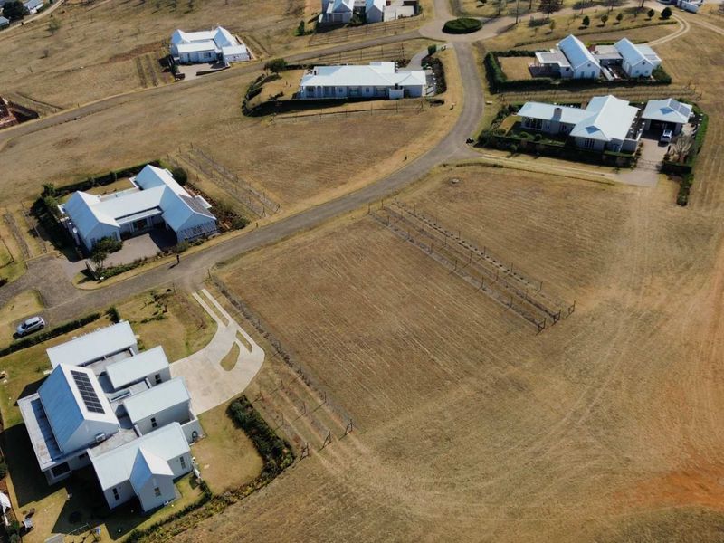 An aerial view of a residential estate featuring multiple detached homes, paved access roads, and open land plots.