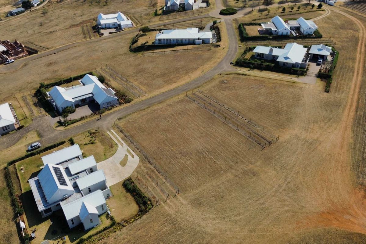 An aerial view of a residential estate featuring multiple detached homes, paved access roads, and open land plots.