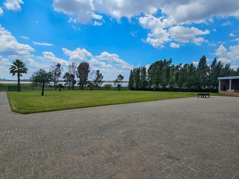 Expansive landscaped garden featuring a large paved driveway, manicured lawn, and scenic water views, providing a serene outdoor setting.