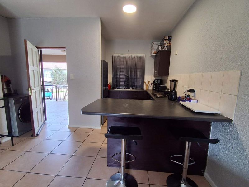 Compact kitchen featuring dark cabinetry, a breakfast bar, tiled backsplash, and direct access to an outdoor balcony area.