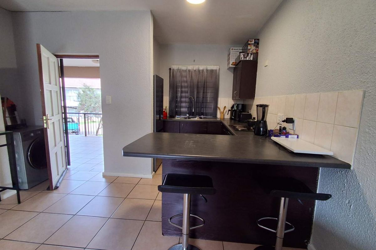 Compact kitchen featuring dark cabinetry, a breakfast bar, tiled backsplash, and direct access to an outdoor balcony area.