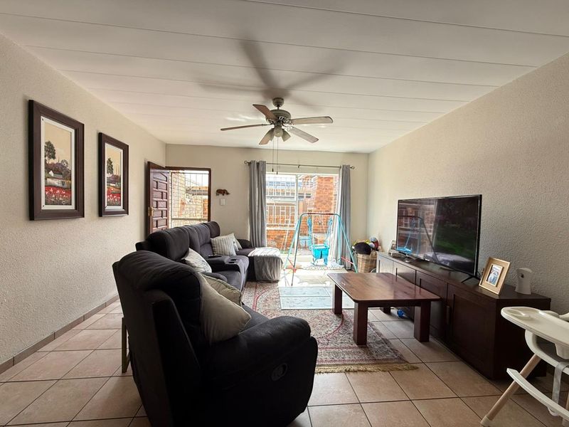 A comfortable living room featuring tiled flooring, a ceiling fan, and a sliding glass door providing access to the outdoor area.