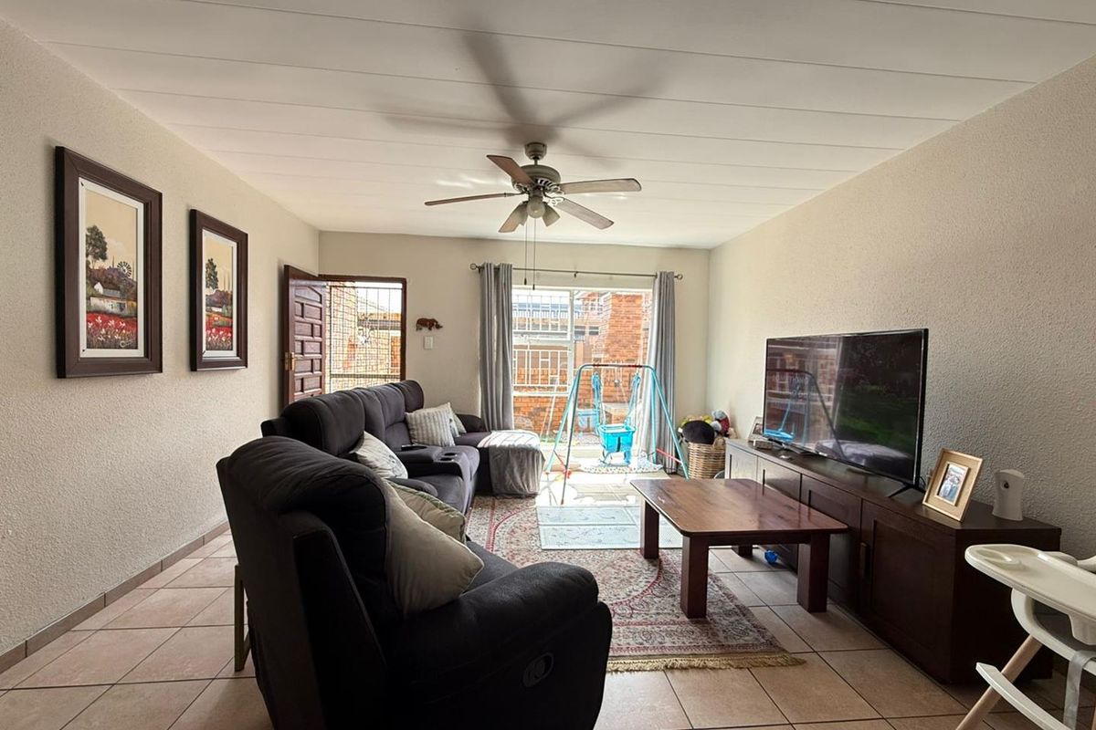 A comfortable living room featuring tiled flooring, a ceiling fan, and a sliding glass door providing access to the outdoor area.