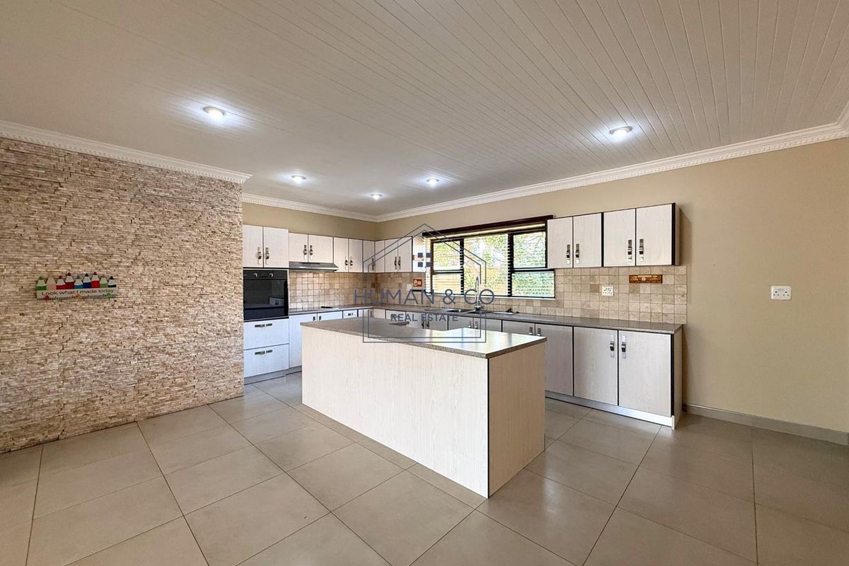 Spacious kitchen featuring a central island, built-in oven, extractor fan, stone-cladding feature wall, and tiled flooring with ample cabinetry.