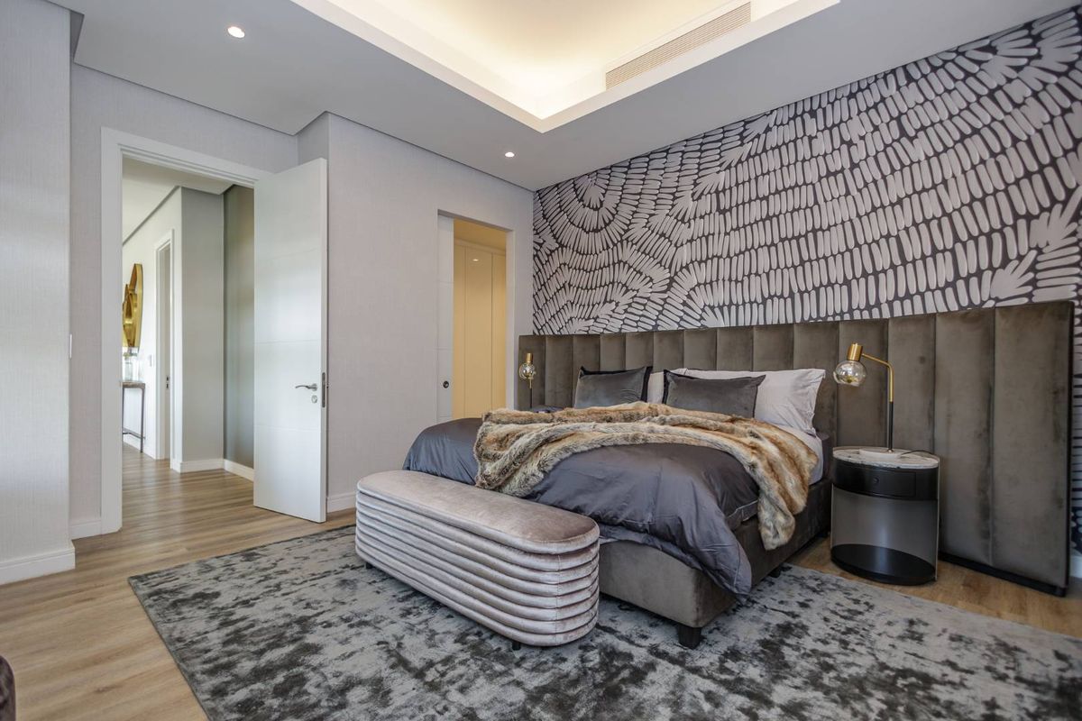 A modern, well-appointed bedroom featuring a custom upholstered headboard, recessed tray ceiling with integrated lighting, and high-quality wood-look flooring.