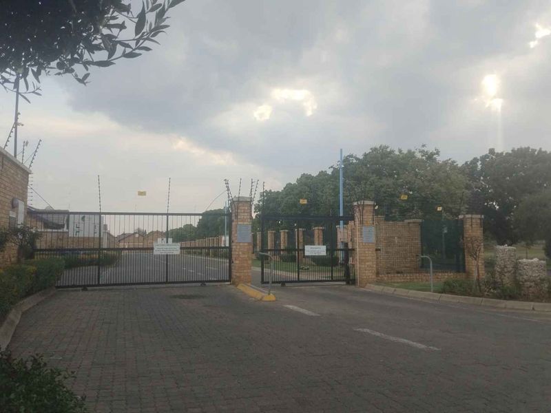 The entrance to the apartment complex features a secure gated access point with electric fencing and brick perimeter walls.