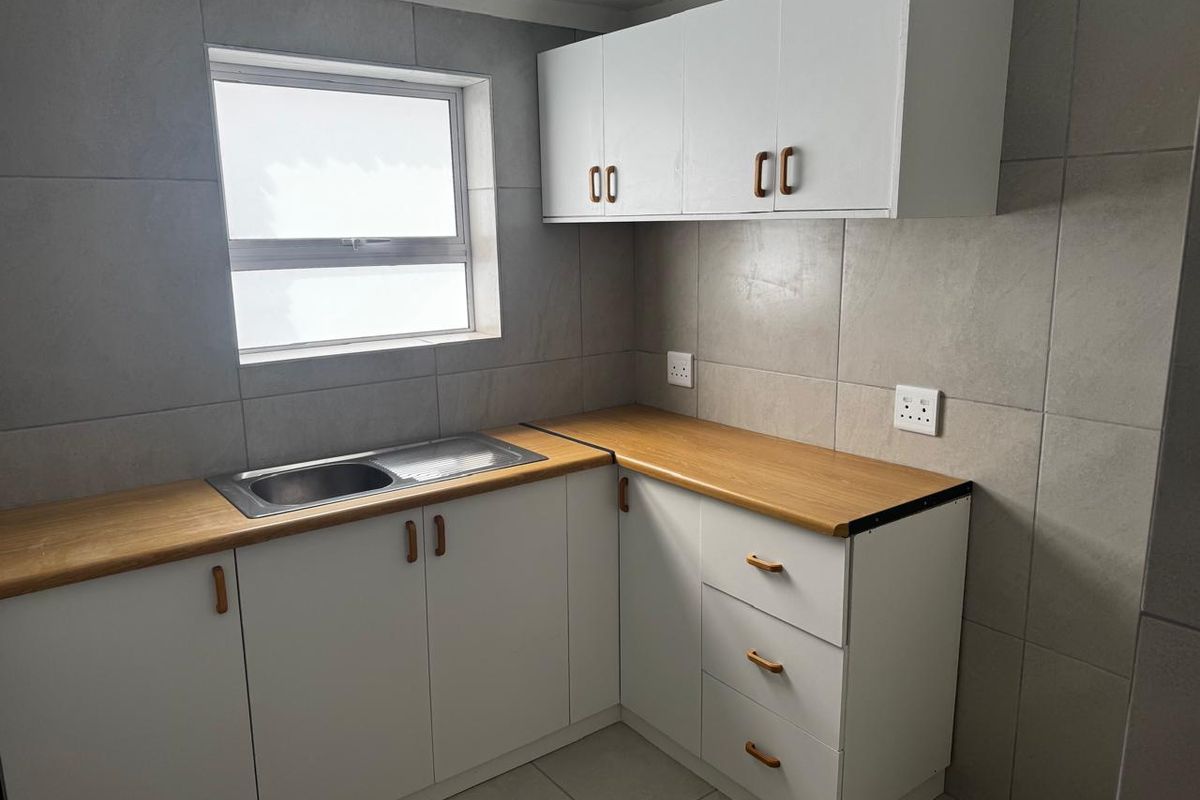 A functional kitchen area featuring white cabinetry, wood-look countertops, a stainless steel sink, and full-height wall tiling.