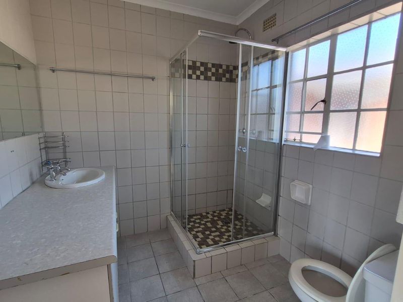 A functional bathroom featuring a shower enclosure, built-in vanity with basin, and toilet, finished with neutral wall and floor tiling.