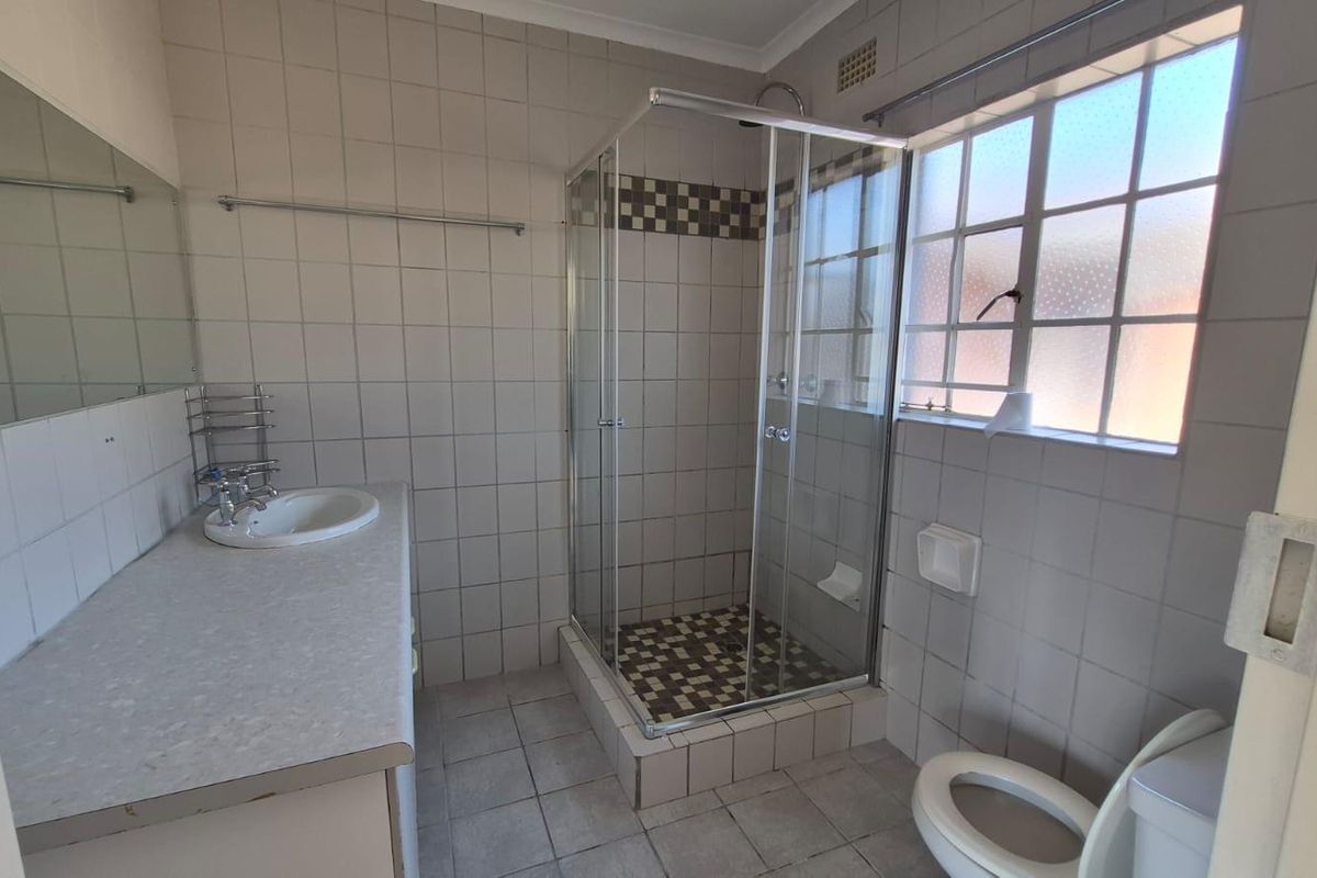 A functional bathroom featuring a shower enclosure, built-in vanity with basin, and toilet, finished with neutral wall and floor tiling.