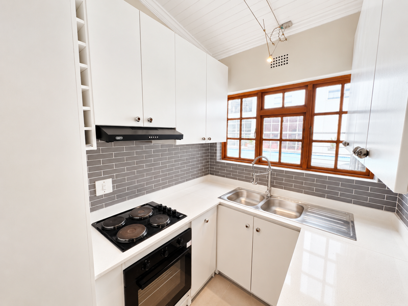 A modern, well-maintained kitchen featuring white cabinetry, stone countertops, a subway tile backsplash, and integrated appliances including an oven and hob.