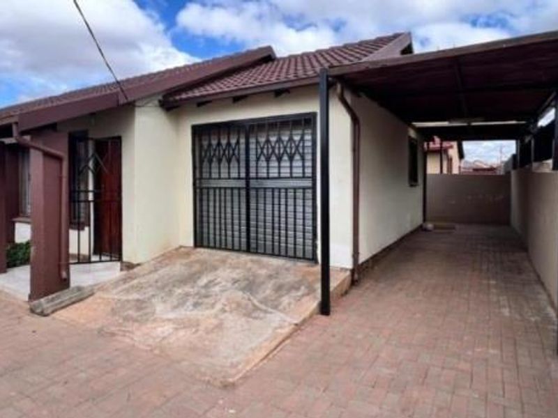 Front exterior view of a house featuring a paved driveway, a covered carport, and secure metal gates.