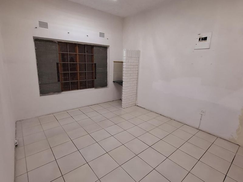 An empty office space featuring tiled flooring, a fluorescent light fixture, and a window with security bars, ready for renovation or custom fit-out.