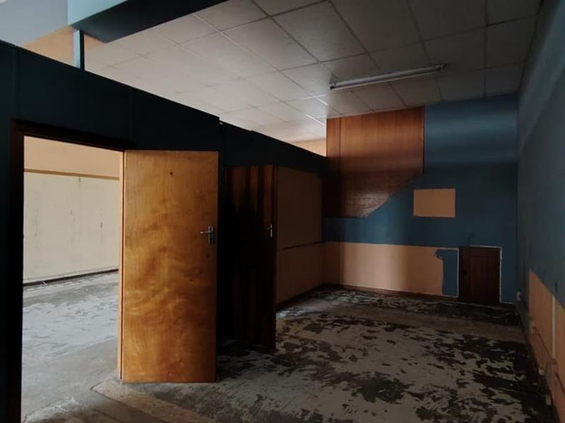 An empty, dated interior space featuring a suspended ceiling, fluorescent lighting, and worn flooring, suitable for renovation or commercial repurposing.
