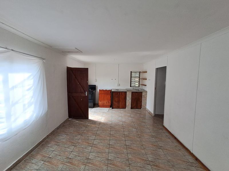 A basic, empty kitchen area featuring tiled flooring, wooden cabinetry, a sink, and a freestanding stove, offering a blank canvas for renovation.