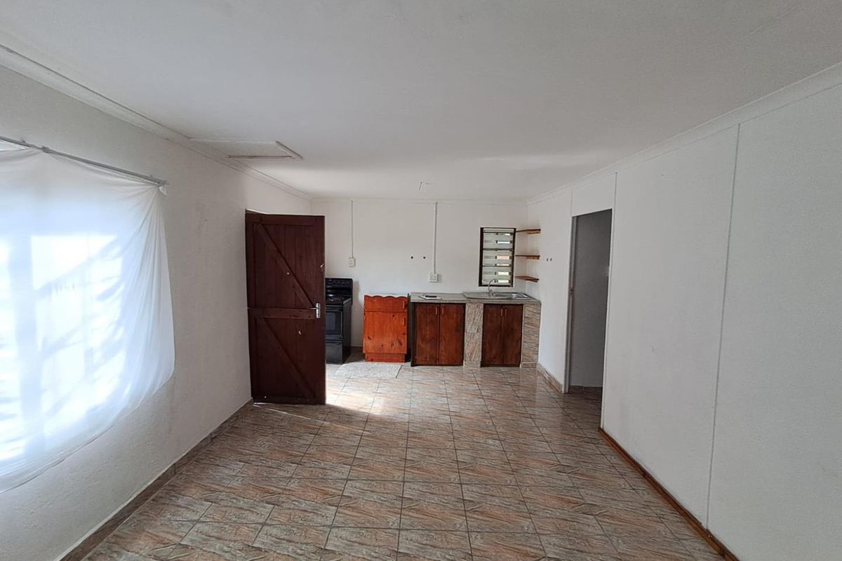 A basic, empty kitchen area featuring tiled flooring, wooden cabinetry, a sink, and a freestanding stove, offering a blank canvas for renovation.