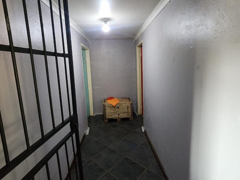 A narrow hallway featuring dark tiled flooring, a security gate, and neutral wall finishes, providing access to adjacent rooms.