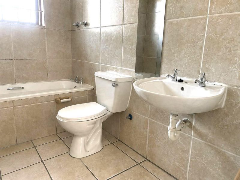 A functional bathroom featuring a built-in bathtub, wall-mounted basin, and toilet, finished with neutral floor-to-ceiling wall tiles.
