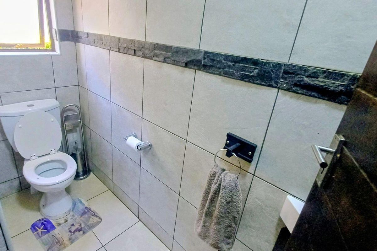 A compact bathroom featuring neutral wall and floor tiles, a decorative stone accent border, and standard sanitary fixtures.