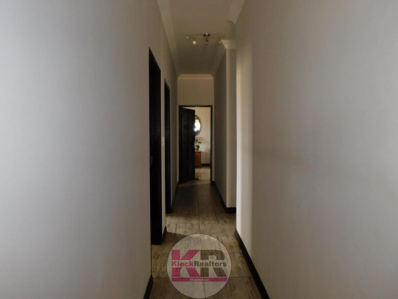 A clean, neutral hallway featuring tiled flooring and dark door frames, providing access to multiple rooms within the home.