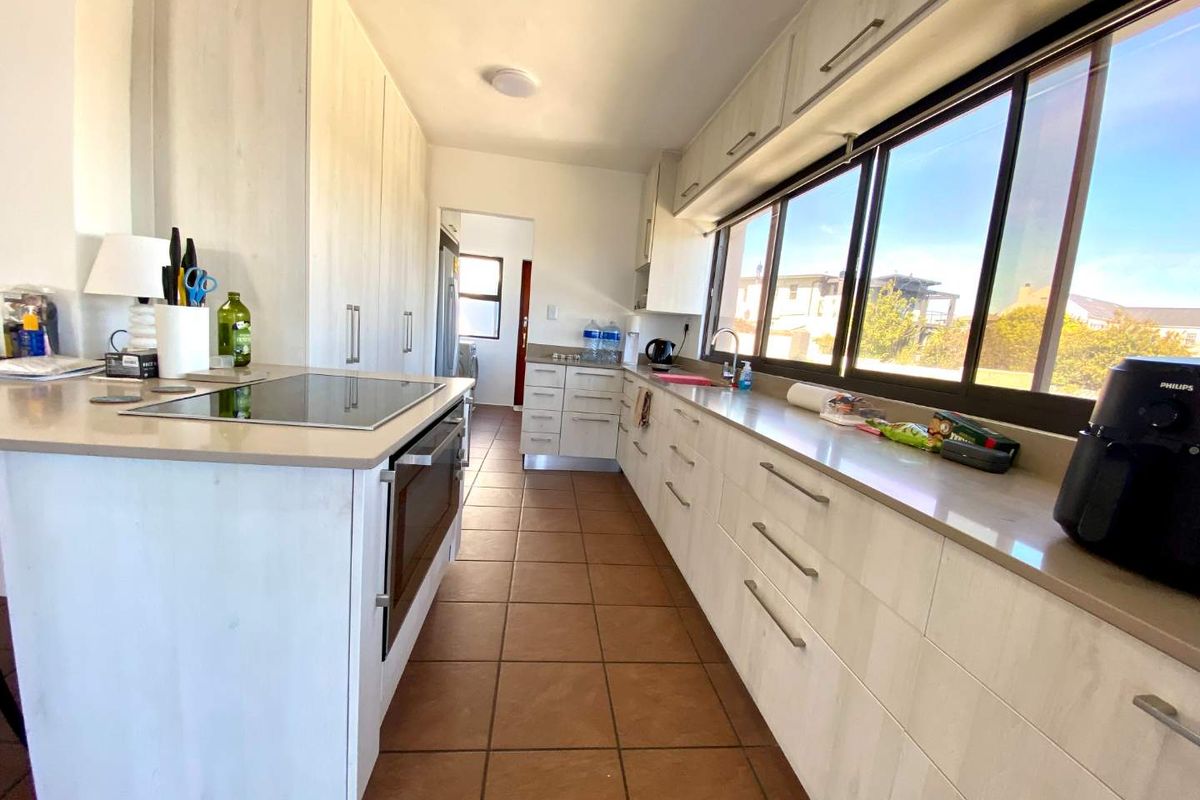 A functional kitchen featuring light-toned built-in cabinetry, stone countertops, an integrated electric hob and oven, and large windows providing ample natural light.