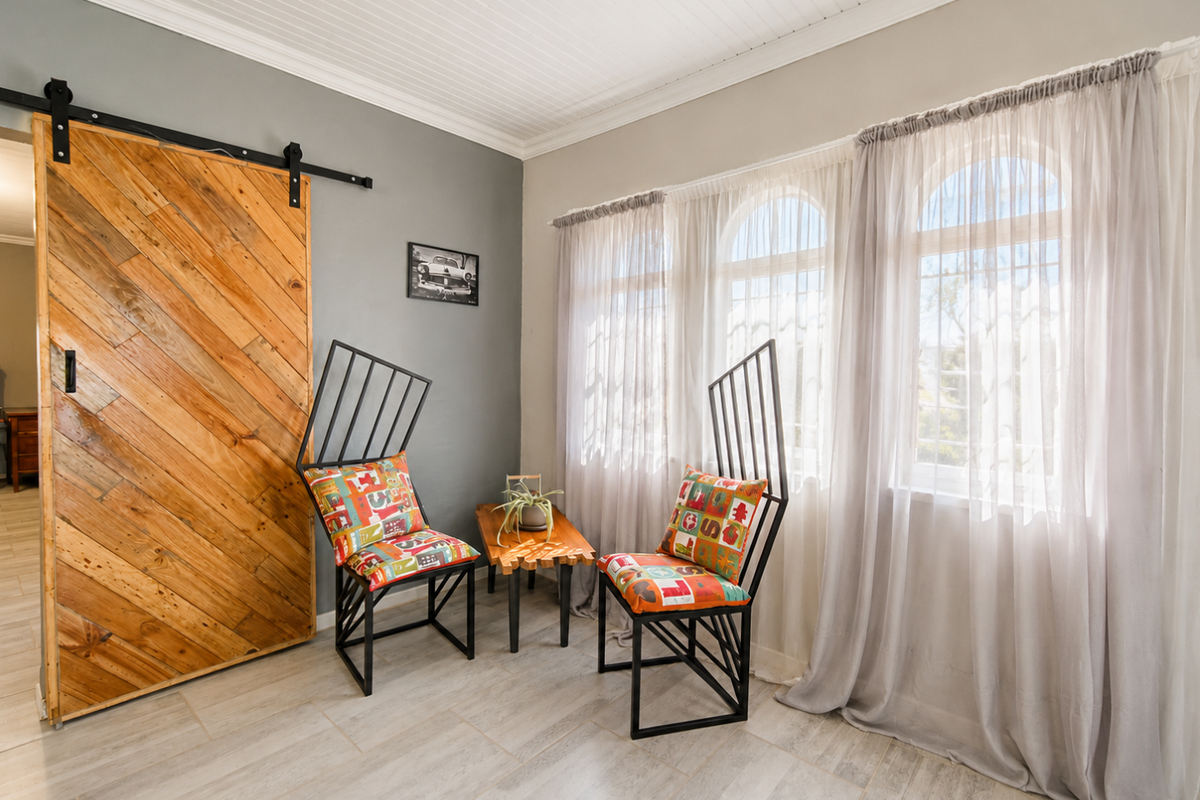 A bright living area featuring a rustic wooden barn-style sliding door, tiled flooring, and arched windows with sheer curtains.