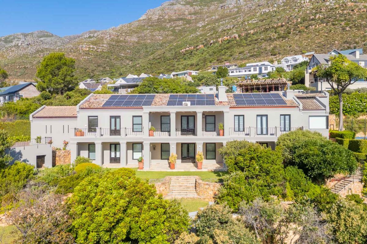 A well-maintained two-story residence featuring a terracotta tiled roof, integrated solar panels, stone landscaping, and a spacious rear balcony overlooking the garden.