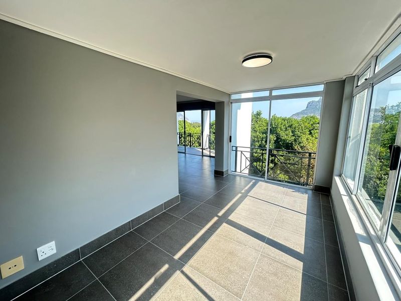 A bright, empty living area featuring large windows, tiled flooring, and direct access to a balcony with scenic views.