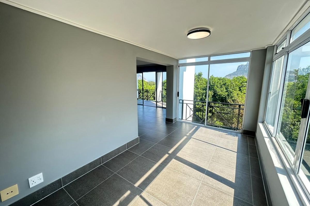 A bright, empty living area featuring large windows, tiled flooring, and direct access to a balcony with scenic views.