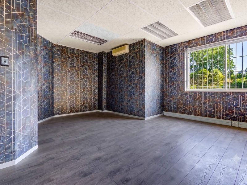 A vacant office space featuring modern laminate flooring, patterned wallpaper, a drop ceiling with recessed lighting, and a wall-mounted air conditioning unit.