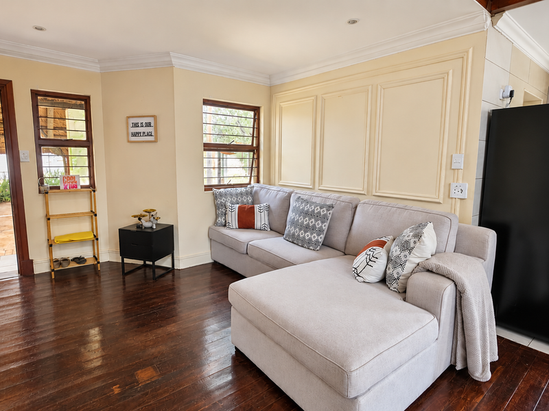 A bright living room featuring dark hardwood flooring, decorative wall paneling, crown molding, and direct access to an outdoor patio area.