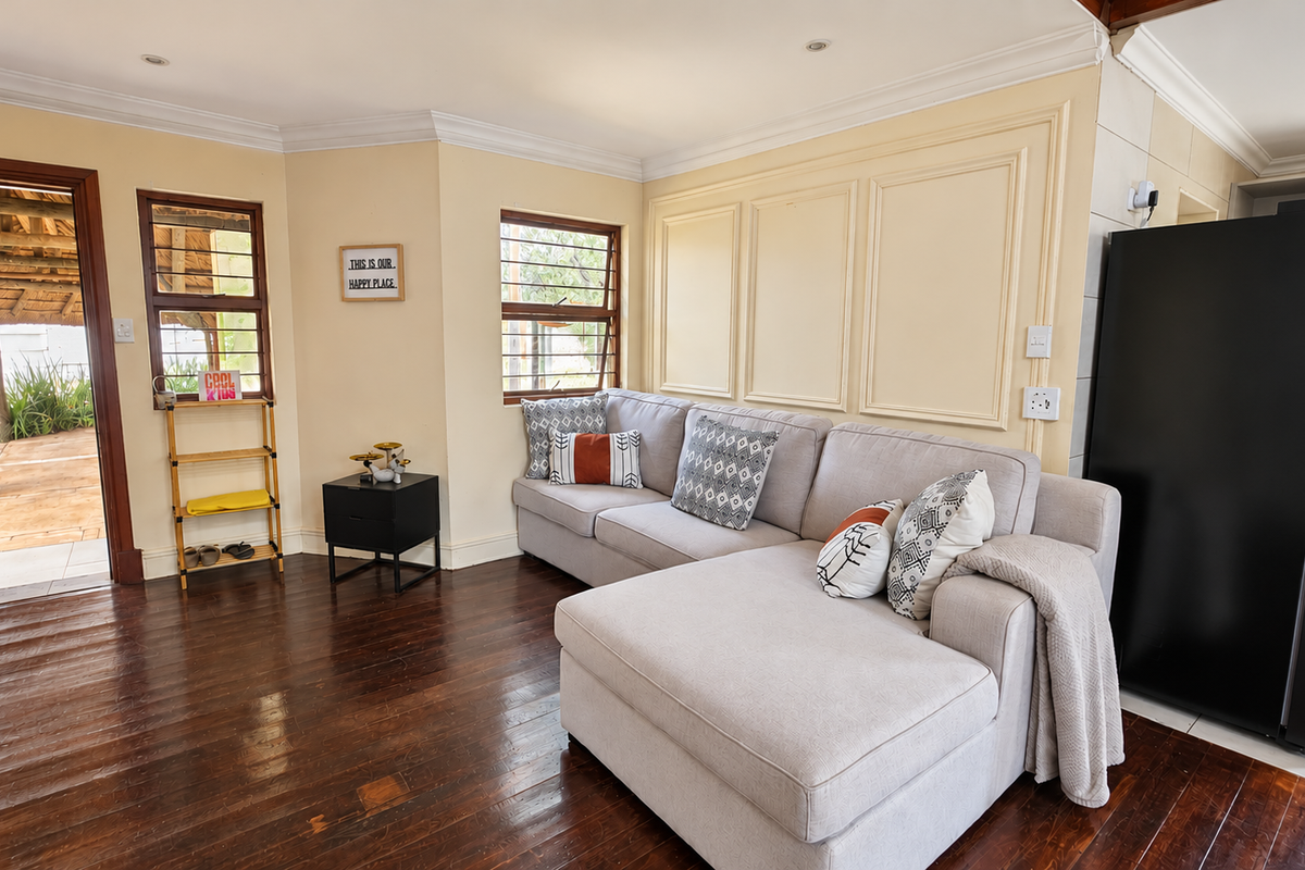 A bright living room featuring dark hardwood flooring, decorative wall paneling, crown molding, and direct access to an outdoor patio area.