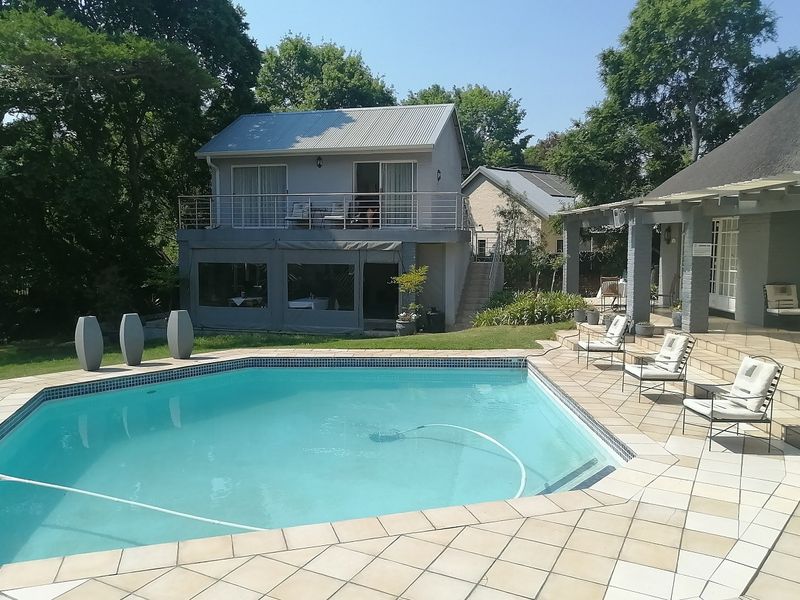 A well-maintained cottage exterior featuring a swimming pool, tiled deck, covered patio area, and a two-story structure with a balcony.