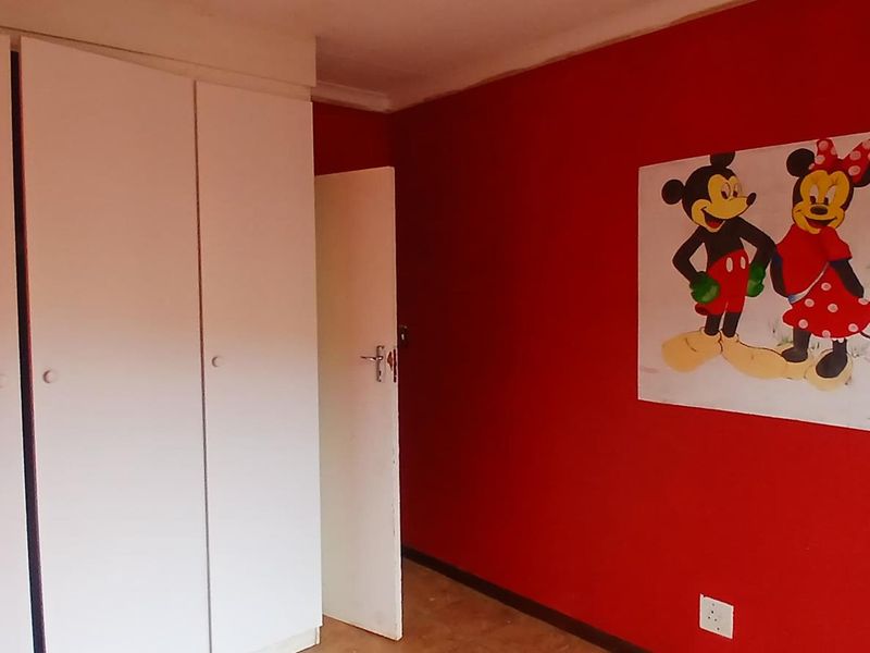 A bedroom featuring built-in cupboards and a bold red accent wall, providing a blank canvas for personalization.