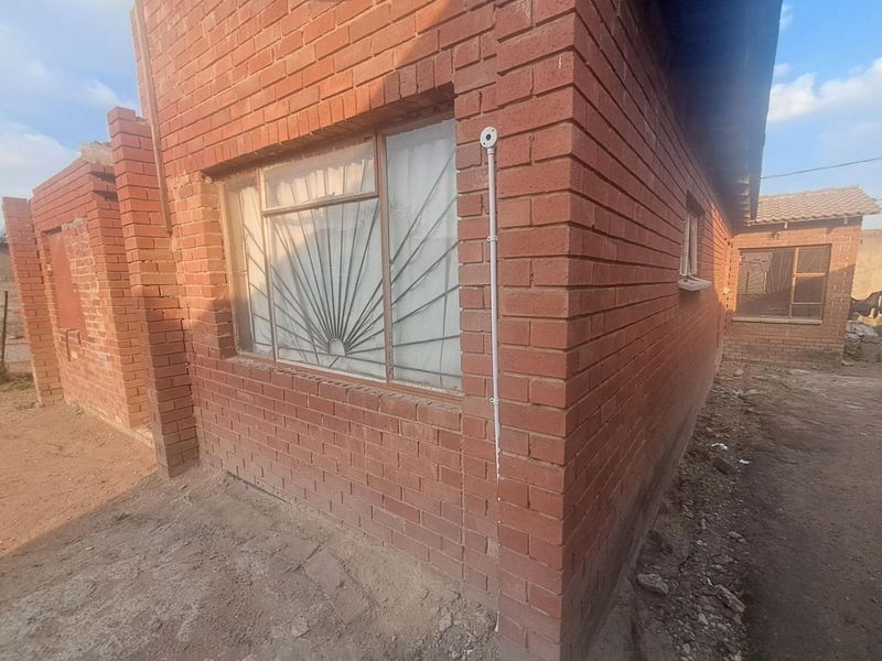 Exterior view of a face brick residential structure featuring metal security bars on windows and exposed external electrical conduit.